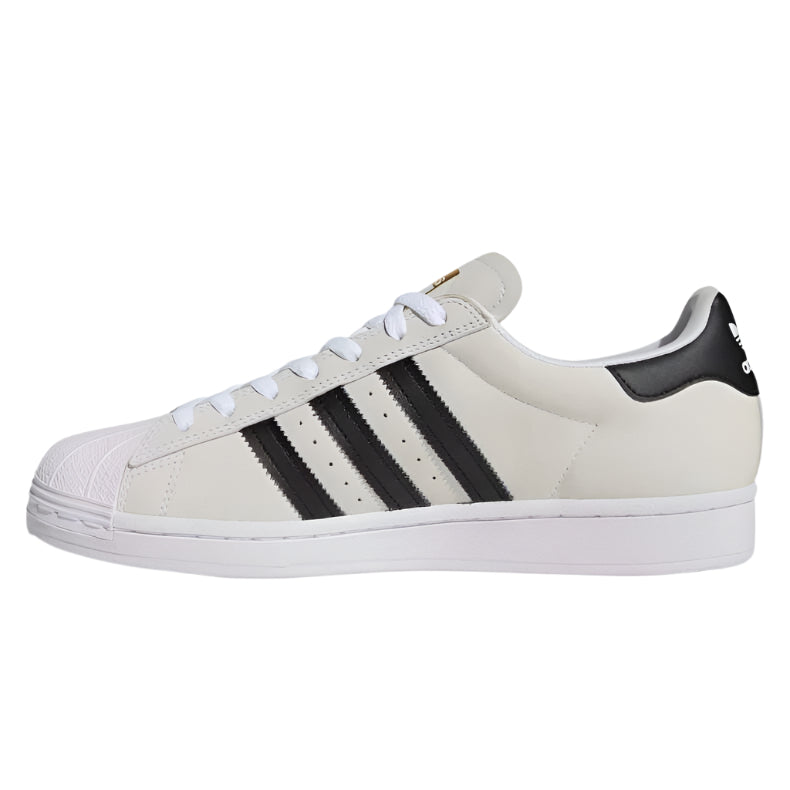Valkoinen Adidas Superstar ADV -kengät, mustat raidat ja kultainen yksityiskohta, ikonisella simpukankärjellä.